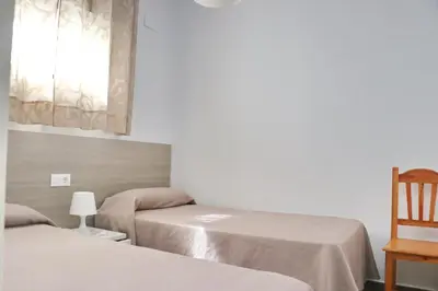 a room with two beds and a chair and a window at Apartamento Canario III in Conil de la Frontera