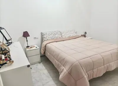 a white bedroom with a bed and a night stand at Playa Fuentebravia apartament in El Puerto de Santa María