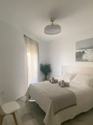 a white bedroom with a bed and a chair at Apartamento Capillera 9 in El Puerto de Santa María