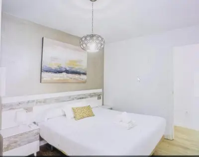 a white bedroom with a bed and a chandelier at Alma gaditana en la caleta in Cádiz