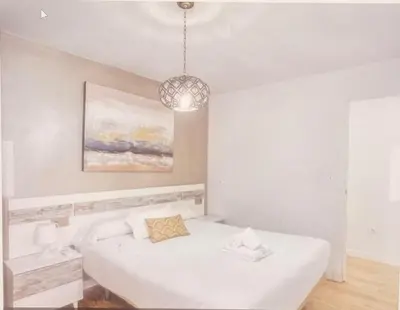 a white bedroom with a bed and a chandelier at Alma gaditana en la caleta in Cádiz