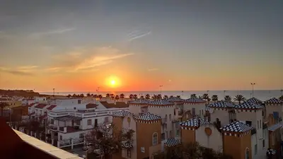 a sunset over a city with buildings and the ocean at Ático Mar in Sanlúcar de Barrameda