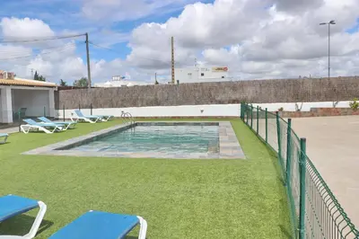 a swimming pool with two blue chairs on the grass at Apartamento Canario IV in Conil de la Frontera
