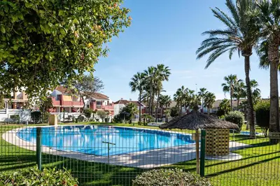 a swimming pool with palm trees and houses at aldea 2 5 1ºB in Chiclana de la Frontera
