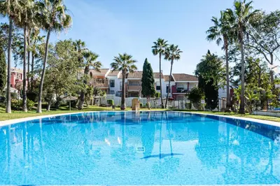 a large blue swimming pool with palm trees at aldea 2 5 1ºB in Chiclana de la Frontera