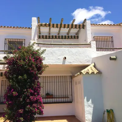 a white house with a gate and a bush with pink flowers at Magnifico apartamento en la Barrosa frente al mar in Novo Sancti Petri