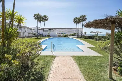 an empty swimming pool with an umbrella and palm trees at Magnifico apartamento en la Barrosa frente al mar in Novo Sancti Petri