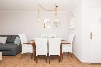 a dining room table with white chairs and a couch at Novo Golf Chiclana in Chiclana de la Frontera