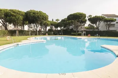 a large blue swimming pool with trees in the background at Estribor in Poblado de Sancti Petri
