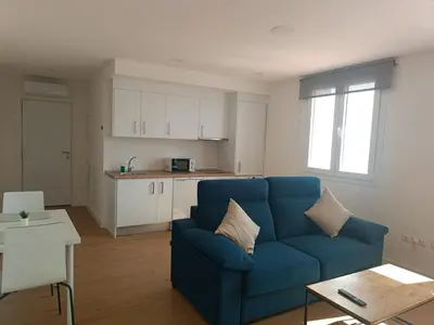a living room with a blue couch and a kitchen at Apartamento La Bota in Jerez de la Frontera