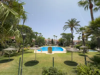 a swimming pool with umbrellas in a park at Dúo de bajos con jardín, juntos y climatizados en Aldea del Coto in Novo Sancti Petri