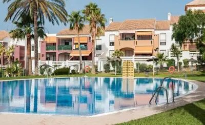 a swimming pool with palm trees and buildings at Dúo de bajos con jardín, juntos y climatizados en Aldea del Coto in Novo Sancti Petri