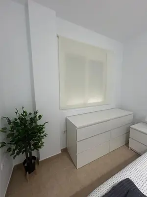 a white bedroom with a window and a plant at Apto cerca de playa Regla con garaje in Chipiona