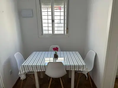 a dining room table with white chairs and a window at Apartamentos Bajo Guía in Sanlúcar de Barrameda