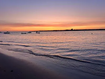 a beach with boats in the water at sunset at Apartamentos Bajo Guía in Sanlúcar de Barrameda
