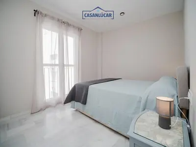 a white bedroom with a bed and a window at Piso Atlantis in Sanlúcar de Barrameda