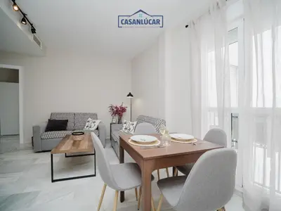 a white living room with a wooden table and chairs at Piso Atlantis in Sanlúcar de Barrameda