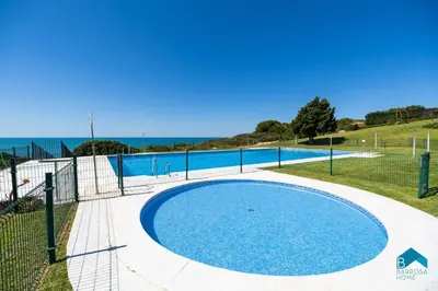 a swimming pool next to a fence and the ocean at Fuente del Sol in Conil de la Frontera