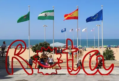 a sign on the beach with many flags at Apartamentos Patio Andaluz El pozito in Rota