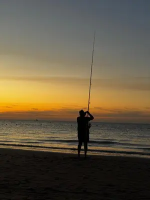 a man standing on the beach holding a fishing rod at La Casita de las Piletas in Sanlúcar de Barrameda