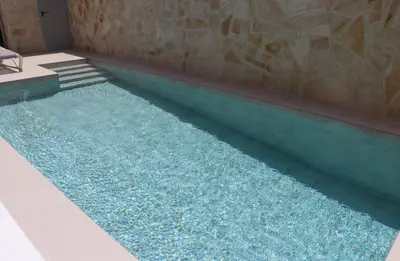 a swimming pool with blue water next to a stone wall at Casa el rincon de la Rosa II in Conil de la Frontera