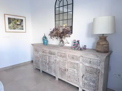 a wooden dresser with a lamp and flowers on it at Luz de Conil is a modern villa next to Playa Fontanilla in Conil de la Frontera