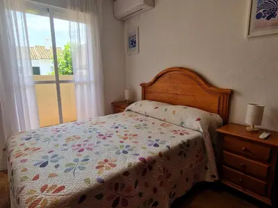 a bedroom with a bed with a floral bedspread and a window at Primera Línea de Playa Casa adosada La Balconera in Chiclana de la Frontera