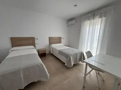 two beds in a room with a table and a window at Alojamientos VICTORIA MAR-CHIPIONA- in Chipiona