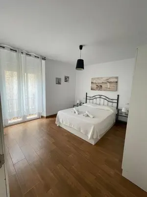 a white bedroom with a white bed and wooden floors at Luz de La Caleta in Cádiz