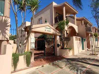 a house with a gate and palm trees at Apartamento Urb Al Andalus A un paseo de la playa de la Barrosa in Novo Sancti Petri