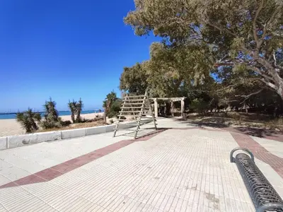 a bench on the side of a beach with a tree at Apartamento Alhaja in El Puerto de Santa María