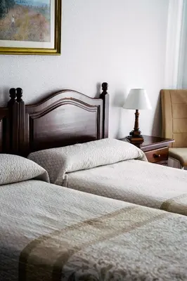 a bedroom with two beds and a table with a lamp at HOTEL Paquita in Chipiona