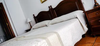 a bed with white sheets and a wooden headboard at HOTEL Paquita in Chipiona