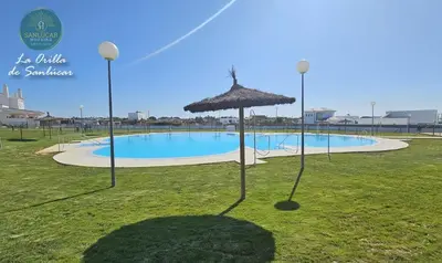 a swimming pool with an umbrella in the grass at La Orilla by Sanlucar Housing in Sanlúcar de Barrameda