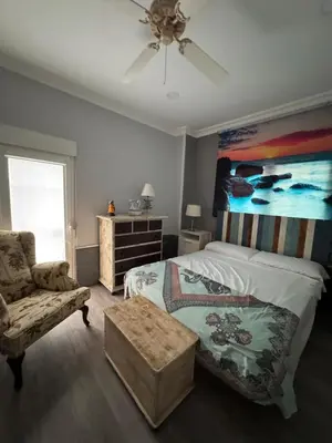 a bedroom with a bed and a chair and a painting at Valdelagrana del Mar in El Puerto de Santa María