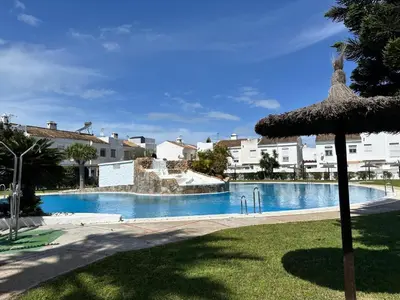 a swimming pool with an umbrella and some buildings at Barrosa Living in Chiclana de la Frontera