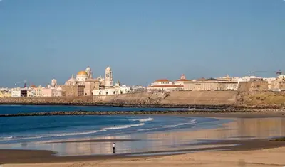 a person walking on the beach with buildings in the background at Casa Keito, Playa y Patio in Cádiz