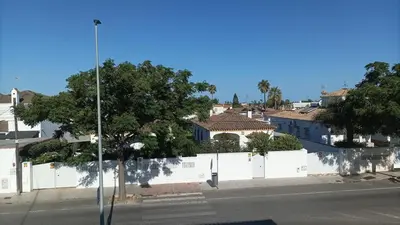 a street with a white fence and trees and buildings at Chiclana Apartamento zona playa in Chiclana de la Frontera