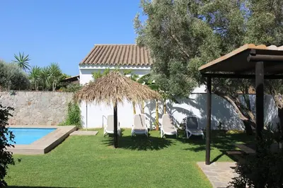 a yard with chairs and an umbrella and a pool at Chalet con piscina privada en Conil in Cádiz