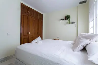 a white bed with two pillows and a wooden door at Playa de fuentebravía in El Puerto de Santa María