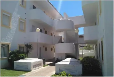 a large white building with two white benches in front of it at Pinar de la Almadraba, Apartamentos Living Sur in Rota