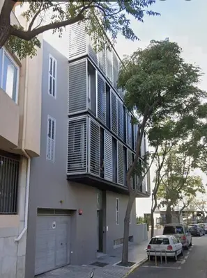 a white building with black shuttered windows and a tree at Apartamento Hibiscos Little Apartments in Cádiz