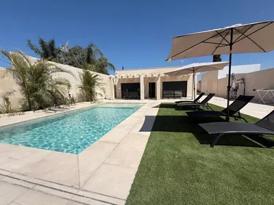 a swimming pool with chairs and an umbrella at Casa Isabel in Chipiona