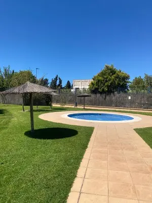 a swimming pool with an umbrella in the grass at Atardeceres en Bajoguía in Sanlúcar de Barrameda
