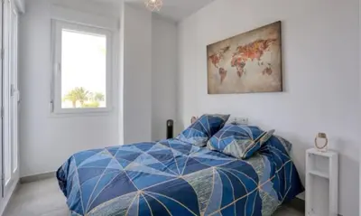 a bedroom with a bed with a blue comforter and a window at Casa Rosado Beautiful House and 60 m of Private Garden in Conil de la Frontera