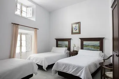 two beds in a room with white walls and windows at Hotel Tugasa Casa Palacio Medina Sidonia in Medina Sidonia