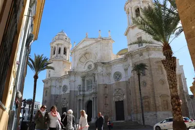 people walking in front of a church with a palm tree at Apartamento Del Rio Playa in Cádiz