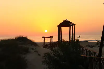a sunset on the beach with the sun in the distance at Apartamento Del Rio Playa in Cádiz