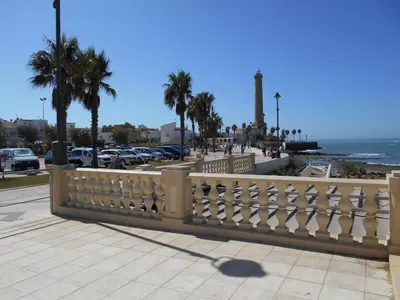 a fence on a sidewalk near the ocean with palm trees at Studio Sleeps 4 with Terrace in Chipiona