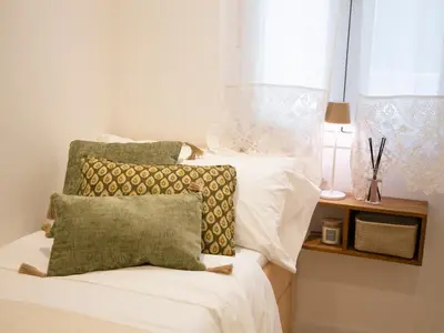a bed with white sheets and green pillows and a window at Hidden Gem GRAN TEATRO FALLA SUITES by ApartmentsinCadiz in Cádiz